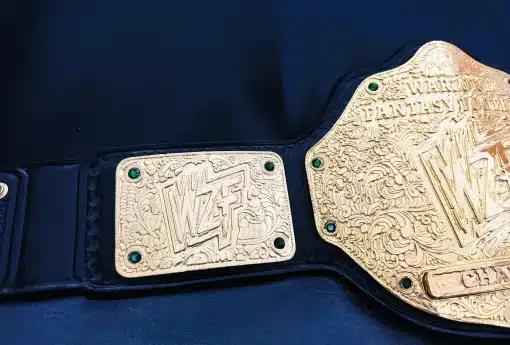 Close-up of custom fantasy football championship belt side plate featuring WZF logo, deep HD engraving, ornate scrollwork, and green crystal accents.