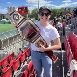 Woman holding a personalized Vermilion Vanguard Player of the Match championship belt at soccer stadium – custom sports trophy.